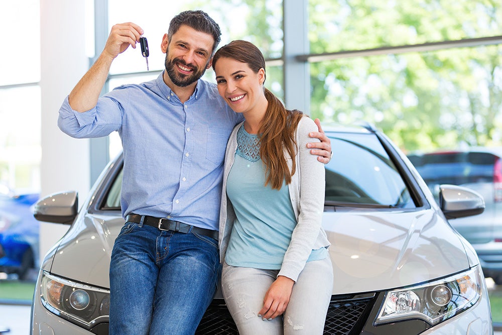 Couple posing in front of their new car with keys in hand - Minocqua Chevrolet in MINOCQUA WI